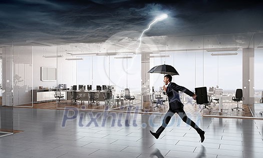 Businessman with umbrella facing storm in modern office. Mixed media