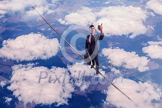 Businessman standing on rope high in sky and doing selfie. Mixed media