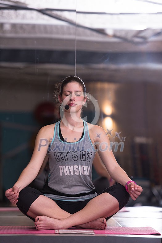 Relaxed young sportswoman doing yoga exercise and meditating in a fitness studio
