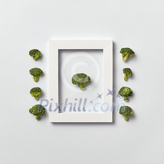 Creative organic composition with freshly picked green broccoli in a frame and out of it on a light gray background, place for text. Flat lay. Vegan concept.