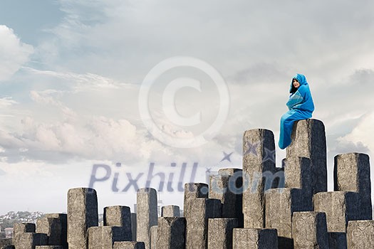 Young woman wrapped in a sleeping bag sitting on edge of stone. Mixed media