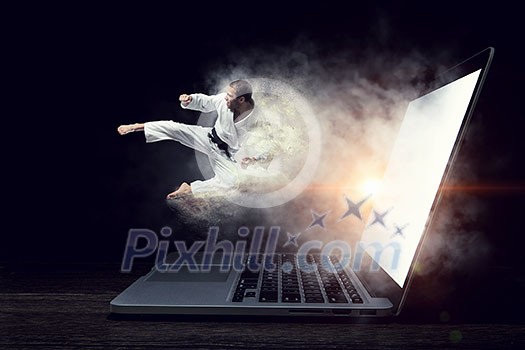 Man karate fighter jumping from laptop screen. Mixed media Man karate fighter jumping from laptop screen. Mixed media