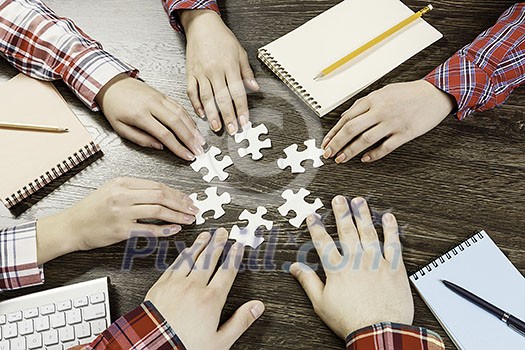 Group of people sitting at table and assembling jigsaw puzzle Group of people sitting at table and assembling jigsaw puzzle