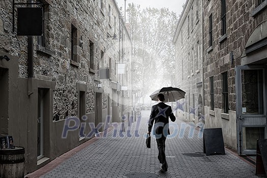 Businessman with black umbrella walking on city street. Mixed media Businessman with black umbrella walking on city street. Mixed media