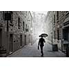 Businessman with black umbrella walking on city street. Mixed media