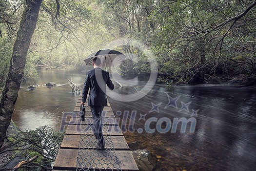 Businessman with umbrella walking alone in forest. Mixed media Businessman with umbrella walking alone in forest. Mixed media