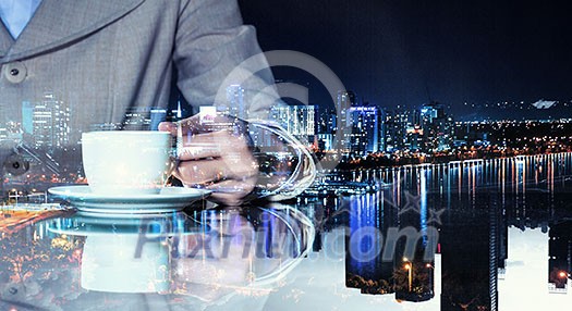 Double exposure of businesswoman hand with coffee cup and modern cityscape