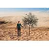 Hipster guy in desert water dry tree. Mixed media