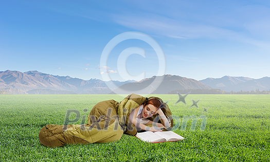 Young woman lying in sleeping bag lying on green grass. Mixed media Young woman lying in sleeping bag lying on green grass. Mixed media