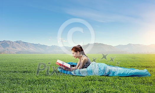 Young woman lying in sleeping bag lying on green grass. Mixed media