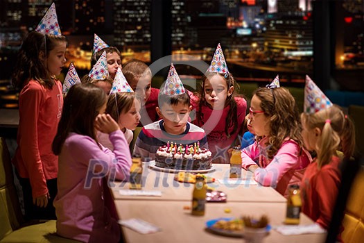 young happy boy and group of his friends having birthday party with a night city through the windows in the background