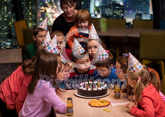 young happy boy and group of his friends having birthday party with a night city through the windows in the background young happy boy and group of his friends having birthday party with a night city through the windows in the background