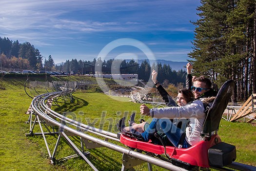 Excited young couple driving alpine coaster while enjoying beautiful sunny day in the nature