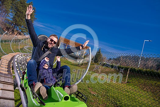 Excited young father and son driving on alpine coaster while enjoying beautiful sunny day in the nature Excited young father and son driving on alpine coaster while enjoying beautiful sunny day in the nature