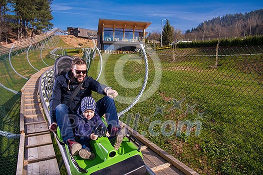 Excited young father and son driving on alpine coaster while enjoying beautiful sunny day in the nature Excited young father and son driving on alpine coaster while enjoying beautiful sunny day in the nature