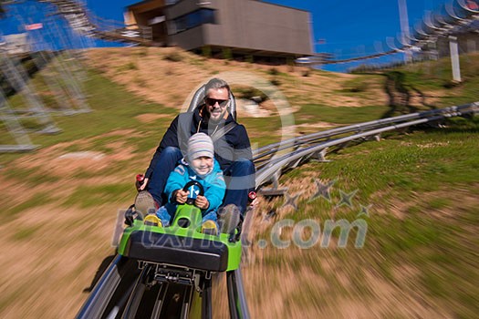 Excited young father and son driving on alpine coaster while enjoying beautiful sunny day in the nature Excited young father and son driving on alpine coaster while enjoying beautiful sunny day in the nature