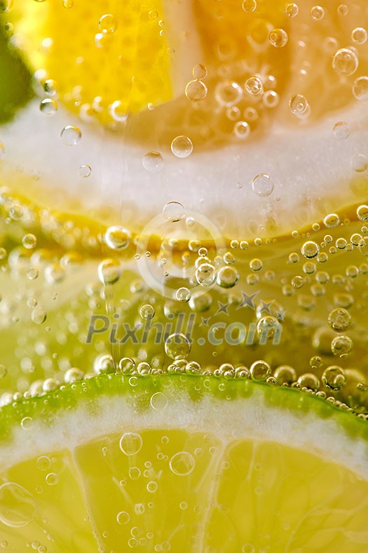 Pieces of citrus fruits of lemon and lime with bubbles in a glass of water. Macro photo of summer drink Pieces of citrus fruits of lemon and lime with bubbles in a glass of water. Macro photo of summer drink