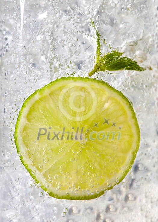Fresh mint leaf and a slice of lime with bubbles in a glass with ice. Macro photo of refreshing drink