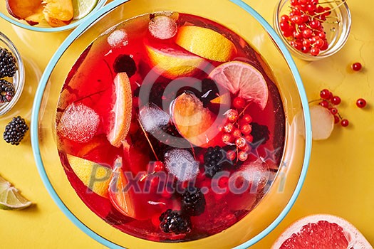 Drink with different berries and fruits with ice cubes in a glass jug presented on a yellow background. Top view Drink with different berries and fruits with ice cubes in a glass jug presented on a yellow background. Top view