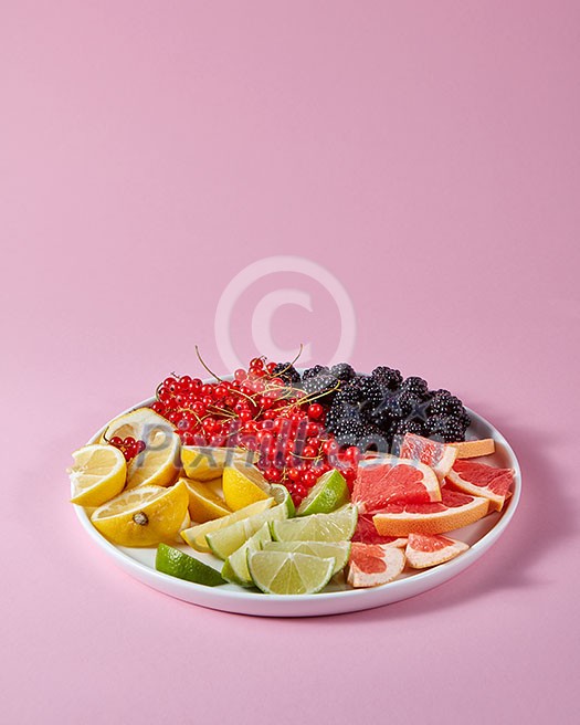 Red currants, mulberries and pieces of lemon, lime, grapefruit in a plate on a pink background with copy space. Set for the preparation of summer vitamin drink