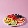 Red currants, mulberries and pieces of lemon, lime, grapefruit in a plate on a pink background with copy space. Set for the preparation of summer vitamin drink