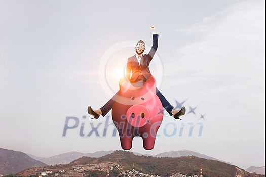 Young cheerful businesswoman flying on pink piggy bank. Mixed media Young cheerful businesswoman flying on pink piggy bank. Mixed media