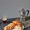 Glass of aromatic hot coffee and plate with freshly baked french croissants on a grey background. Continental breakfast concept. Place for text.