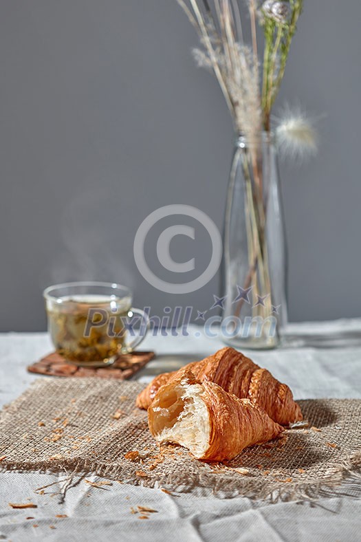 Delicious morning breakfast setting with french homemade pastry, cup of green aromatic fresh tea and flower's vase on a grey textile background. Place for text.
