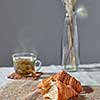 Delicious morning breakfast setting with french homemade pastry, cup of green aromatic fresh tea and flower's vase on a grey textile background. Place for text.