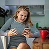 Teenage girl using her cell phone, being angry, while having a cup of tea in modern kitchen setting (shalllow DOF, color toned image)