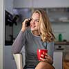 Teenage girl calling on her cell phone while having a cup of tea in modern kitchen setting (shalllow DOF, color toned image)
