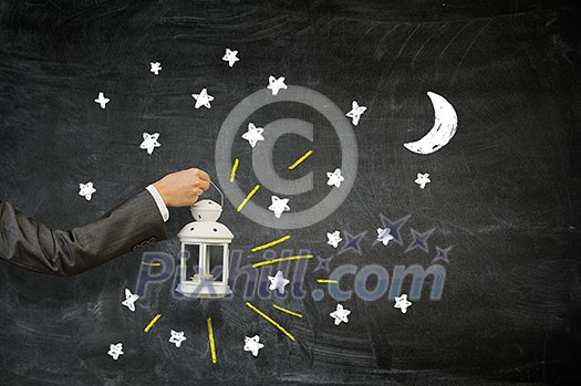 Hand of person holding lantern against chlkboard background Hand of person holding lantern against chlkboard background