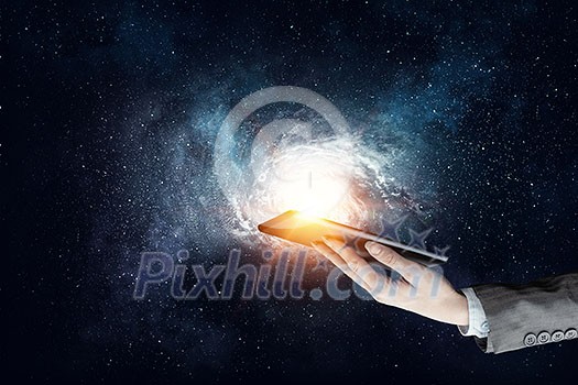 Businesswoman holding tablet computer against galaxy background. Mixed media