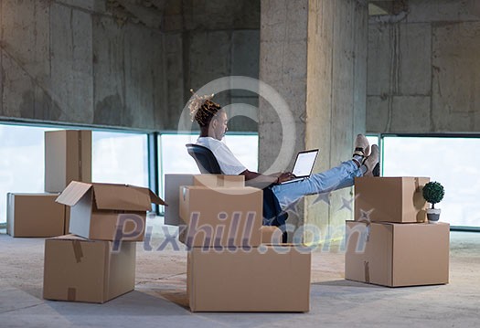 young african american male architect on construction site checking documents and business workflow using laptop computer with cardboard boxes around him in new startup office