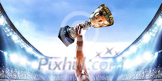 Hand of athlete holding cup trophy against stadium. Mixed media Hand of athlete holding cup trophy against stadium. Mixed media