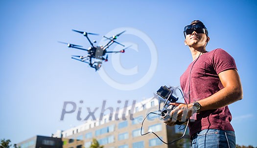 Handsome young man flying a drone outdoors using a VR/augmented reality glasses to operate the device, to see in real time the video feed from the drone