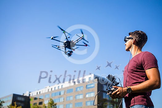 Handsome young man flying a drone outdoors using a VR/augmented reality glasses to operate the device, to see in real time the video feed from the drone