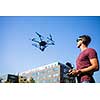 Handsome young man flying a drone outdoors using a VR/augmented reality glasses to operate the device, to see in real time the video feed from the drone