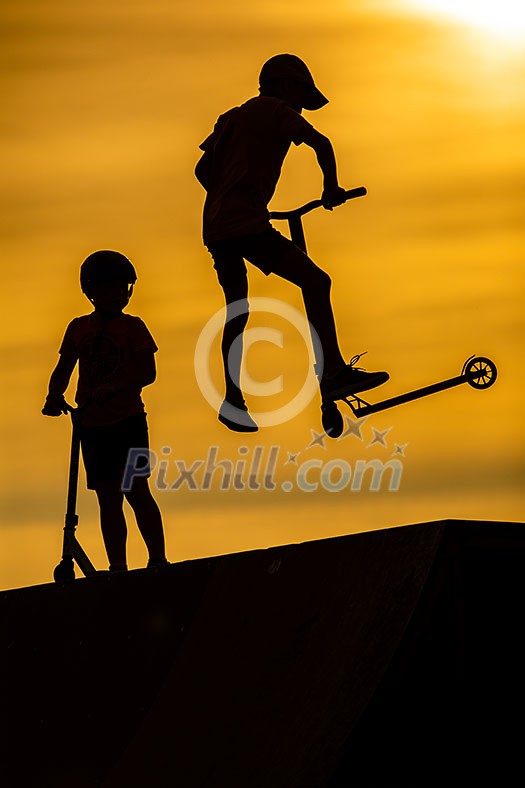 Silhouette of little boys riding scooters against the background of a sea sunset