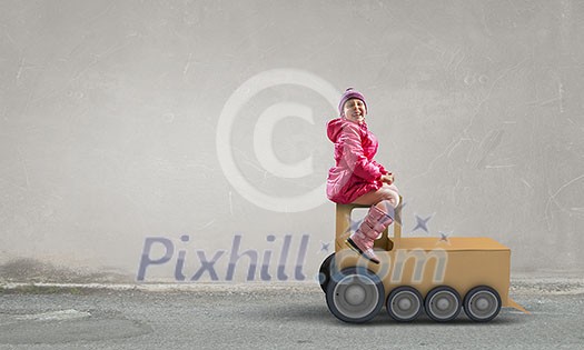 Little girl playing with cardboard train on concrete wall background Little girl playing with cardboard train on concrete wall background
