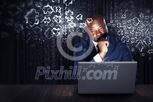 Handsome afroamerican businessman sitting at desk and working on laptop. Mixed media