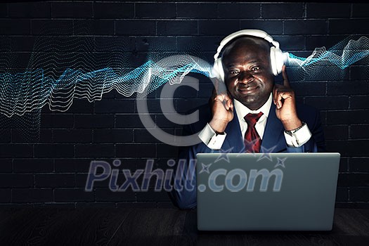 Handsome afroamerican businessman sitting at desk and working on laptop. Mixed media