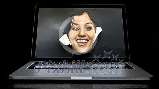 Face of young curious woman peeking through a hole in laptop screen. Mixed media