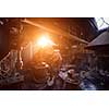 traditional blacksmith manually forging the red hot molten metal on the anvil with sunlight through the windows in smithy workshop. Blacksmith working metal with hammer in the forge