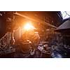 traditional blacksmith manually forging the red hot molten metal on the anvil with sunlight through the windows in smithy workshop. Blacksmith working metal with hammer in the forge