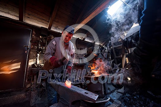 blacksmith manually forging the red hot molten metal on the anvil in traditional smithy workshop. Blacksmith working metal with hammer in the forge blacksmith manually forging the red hot molten metal on the anvil in traditional smithy workshop. Blacksmith working metal with hammer in the forge