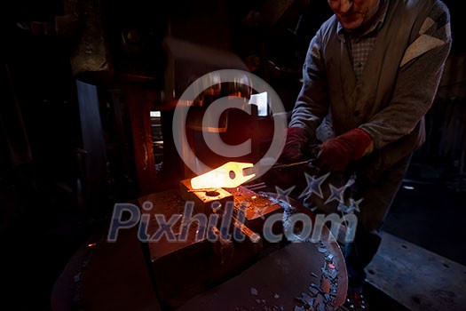 blacksmith manually forging the red hot molten metal on the anvil in traditional smithy workshop. Blacksmith working metal with hammer in the forge blacksmith manually forging the red hot molten metal on the anvil in traditional smithy workshop. Blacksmith working metal with hammer in the forge