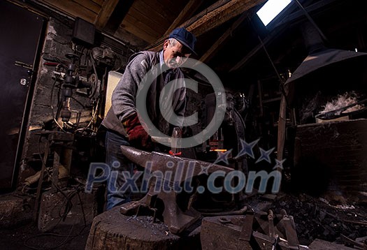 blacksmith manually forging the red hot molten metal on the anvil in traditional smithy workshop. Blacksmith working metal with hammer in the forge blacksmith manually forging the red hot molten metal on the anvil in traditional smithy workshop. Blacksmith working metal with hammer in the forge