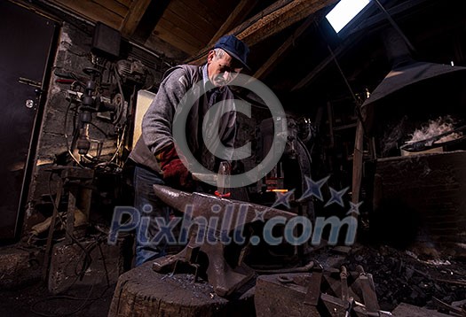 blacksmith manually forging the red hot molten metal on the anvil in traditional smithy workshop. Blacksmith working metal with hammer in the forge