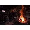 young traditional Blacksmith working with open fire  The blacksmith making flames in smithy with spark fireworks forging hot iron in workshop